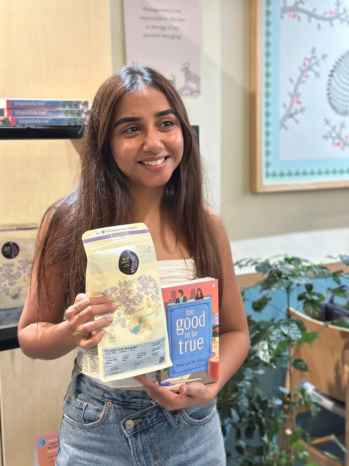 Author Prajakta Koli holding a Blue Tokai Coffee Roasters bag labelled “Too Good To Be True Blend” alongside a copy of her novel Too Good To Be True.